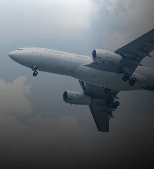 Um grande avião comercial, usado para transporte de cargas aéreas, voa em um céu nublado com o trem de pouso estendido, visto de baixo e ligeiramente para o lado.