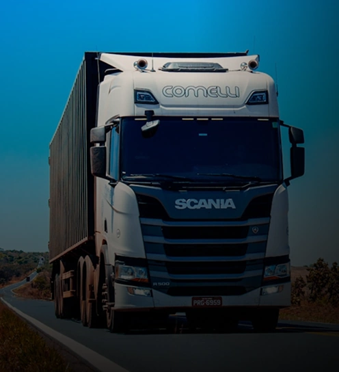 Um semi-caminhão branco usado para transporte de carga rodoviário, com um grande reboque de carga, dirige em uma estrada rural sob um céu azul claro.
